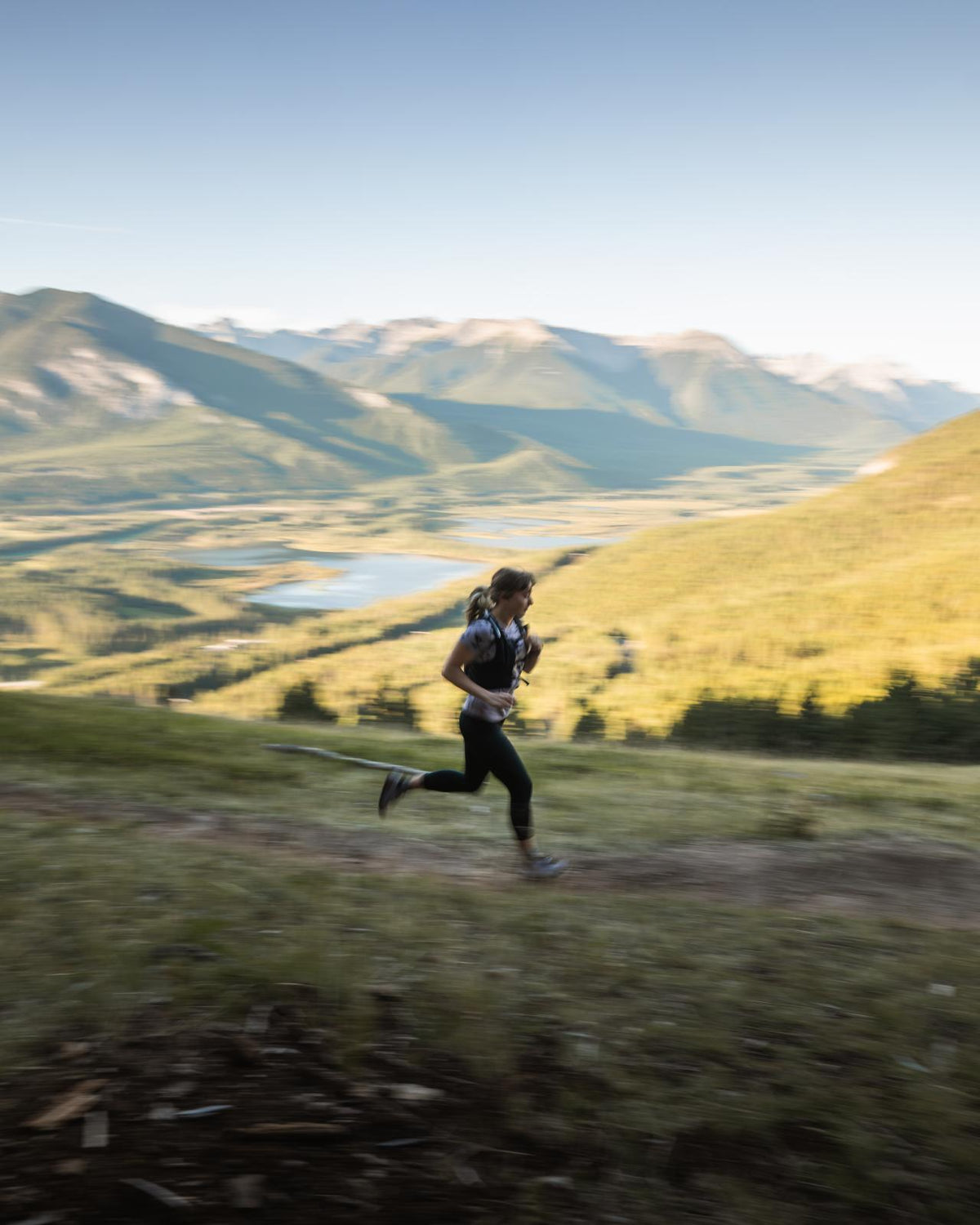 Person running on a trail with mountains and a lake in the background